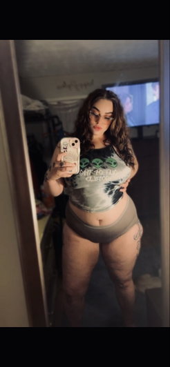 Woman in crop top and underwear taking mirror selfie in dimly lit room.
