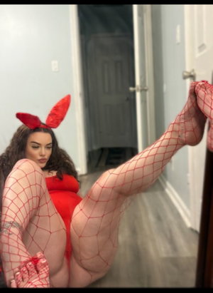 Woman in red lingerie and fishnet stockings posing indoors with red devil ears.