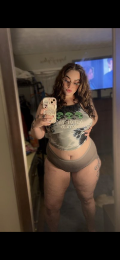 Woman in crop top and underwear taking mirror selfie in bedroom.
