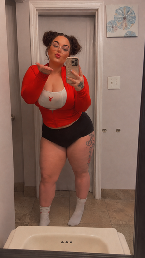 Curvy woman in red jacket taking mirror selfie in bathroom.