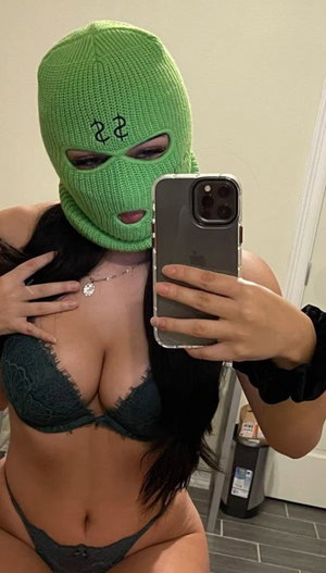 Woman in green balaclava and lace lingerie taking mirror selfie indoors.