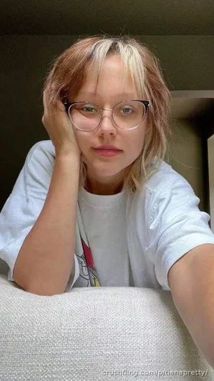 Woman with short blonde hair and glasses wearing a white t-shirt, resting her head on her hand