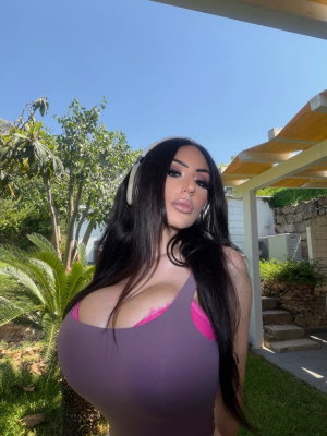Woman with long dark hair in purple top outdoors.