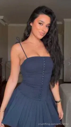 Woman with long dark hair in a navy blue strapless dress, standing indoors.