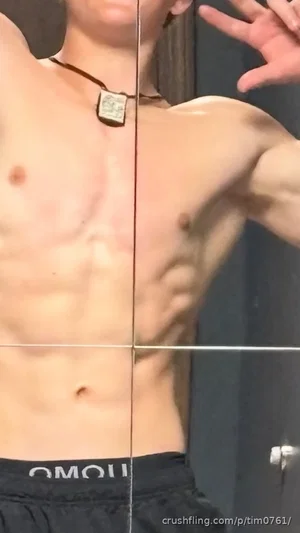 Shirtless muscular man in black shorts posing in front of mirror.