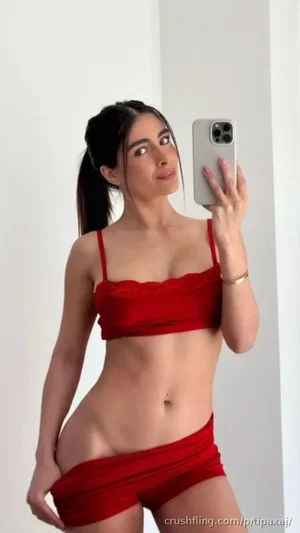 Woman in red lingerie taking mirror selfie, indoor setting.