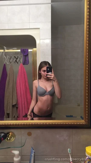 Woman in gray bra and black underwear takes mirror selfie in bathroom.