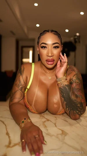 Woman with tattoos wearing colorful lingerie, lying on marble surface indoors.