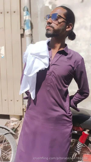 Man in purple shirt with white cloth draped over shoulder, standing outdoors near motorcycle.