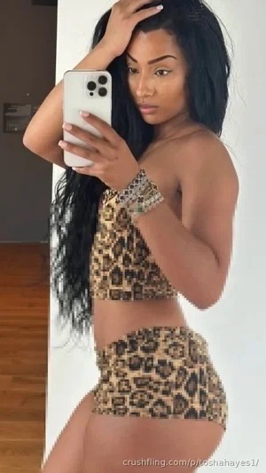 Woman with long black hair in leopard print top and shorts, taking mirror selfie indoors.