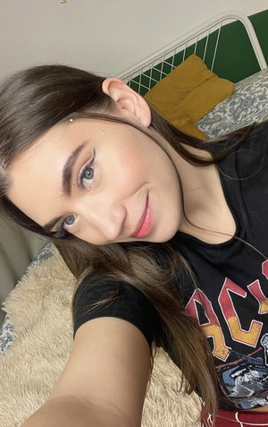 Woman with brown hair and makeup in black graphic tee, lying on bed with fluffy blanket.