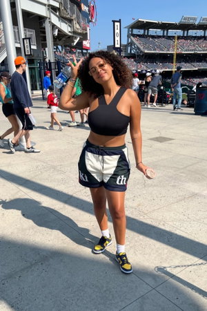 Woman with curly hair in black top and shorts at stadium.