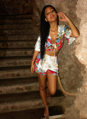 Woman with long braids in floral crop top and shorts on stairs.