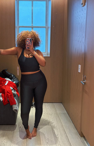Curvy woman with curly hair taking mirror selfie in black activewear indoors.