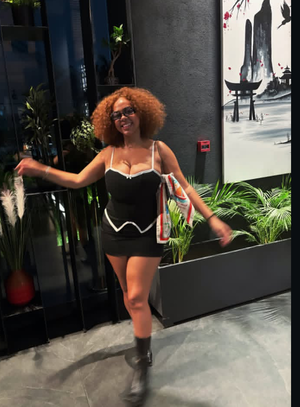 Curvy woman with curly hair in black mini dress posing indoors.