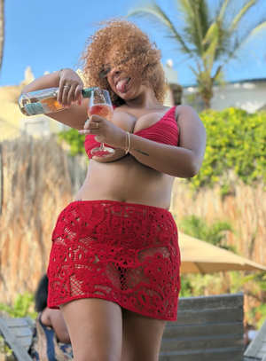 Curvy woman in red lace skirt pouring drink outdoors.