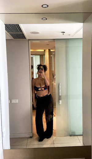 Woman in patterned bra and black pants taking mirror selfie in modern indoor space.