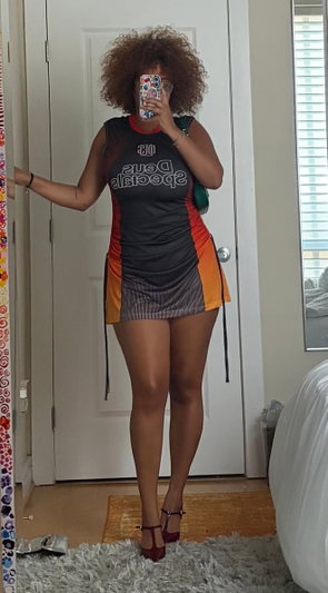 Woman with curly hair in a black and orange dress, taking mirror selfie indoors.