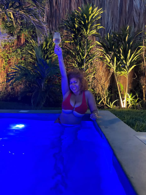 Woman in red bikini holds glass in lit pool at night.