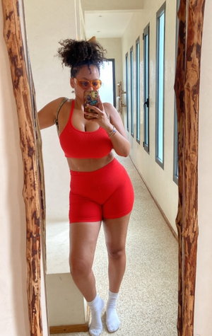 Woman in red athletic wear taking mirror selfie in hallway.