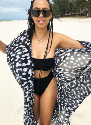 Woman in black bikini and patterned cover-up on beach.