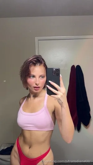 Woman in pink crop top and red underwear taking mirror selfie in bedroom.