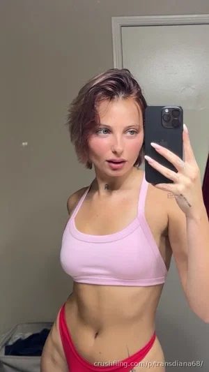 Woman in pink sports bra and red underwear taking mirror selfie indoors.