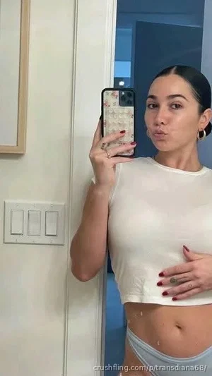 Woman in white crop top and light blue underwear takes mirror selfie in indoor setting.