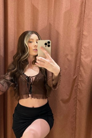 Woman with wavy hair in sheer top and mini skirt in dressing room.