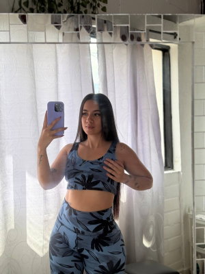 Curvy woman with long dark hair in patterned activewear taking mirror selfie.