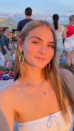 Woman with blonde hair and colorful earrings in a white strapless top at an outdoor event.