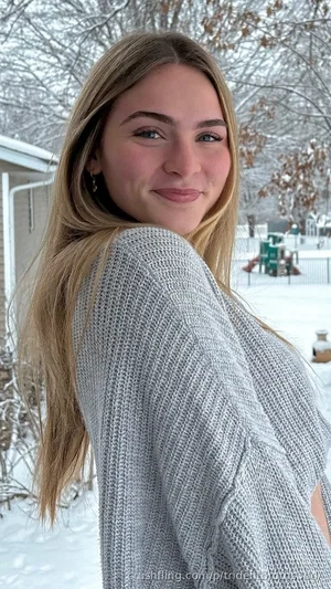 Woman with blonde hair in a gray sweater outdoors in snow.
