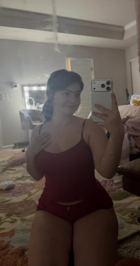 Woman in red lingerie taking mirror selfie in bedroom.