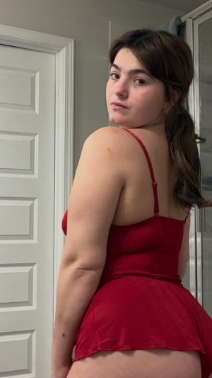 Curvy brunette in red dress posing indoors near door.