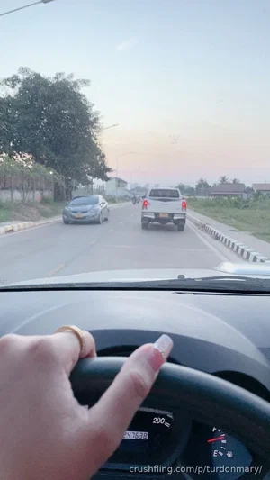Hand on steering wheel, driving on road during dusk, cars ahead.