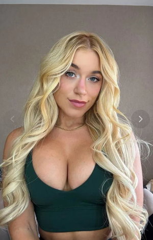 Blonde woman with long wavy hair wearing green top indoors.