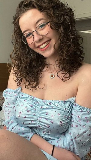 Woman with curly brown hair and glasses in blue floral top.