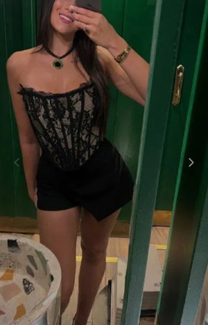 Woman in black lace top and shorts taking mirror selfie indoors.