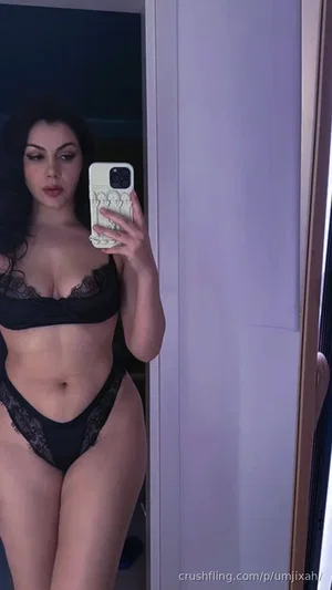 Woman in black lace lingerie taking mirror selfie in indoor setting.