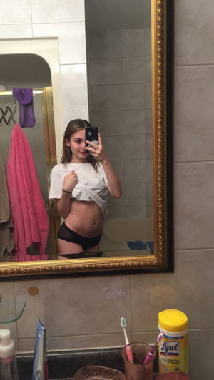 Woman in white shirt and black underwear takes mirror selfie in bathroom.