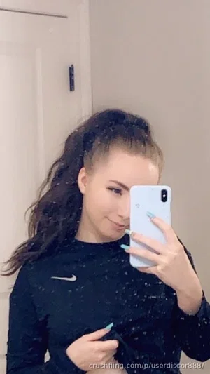 Woman with dark hair in high ponytail, wearing black long-sleeve top, taking mirror selfie indoors.