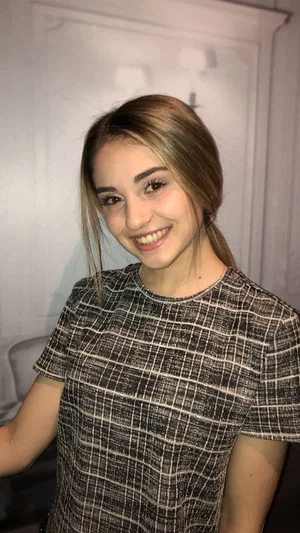 Woman with light brown hair in a plaid top, smiling indoors.