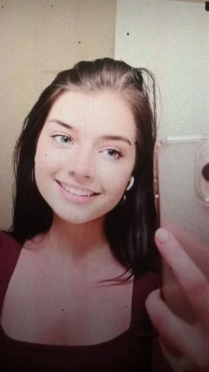 Woman with dark hair in a dark top taking a mirror selfie indoors.
