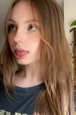 Woman with wavy blonde hair, tongue out, dark shirt, indoor.