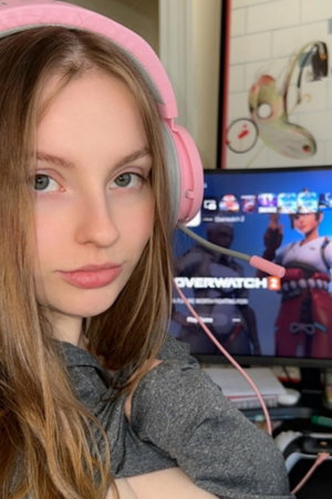 Woman in gray hoodie and pink headphones at gaming desk.