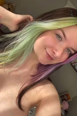 Woman with multicolored hair taking a topless selfie indoors.