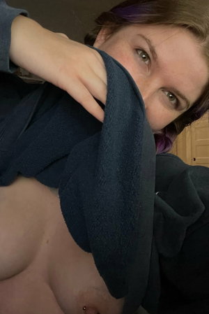 Woman with purple hair in blue hoodie taking indoor selfie.