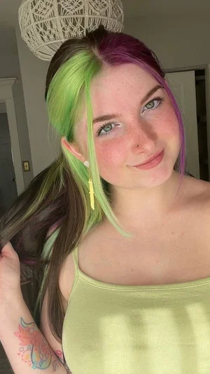Woman with colorful hair, green top, tattoo on arm, indoors.