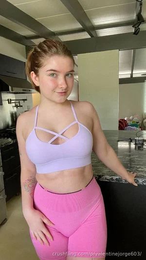 Woman in lavender sports bra and pink shorts posing in kitchen.