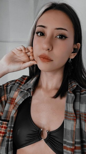 Slim Asian woman with split hair in open plaid shirt over black top.